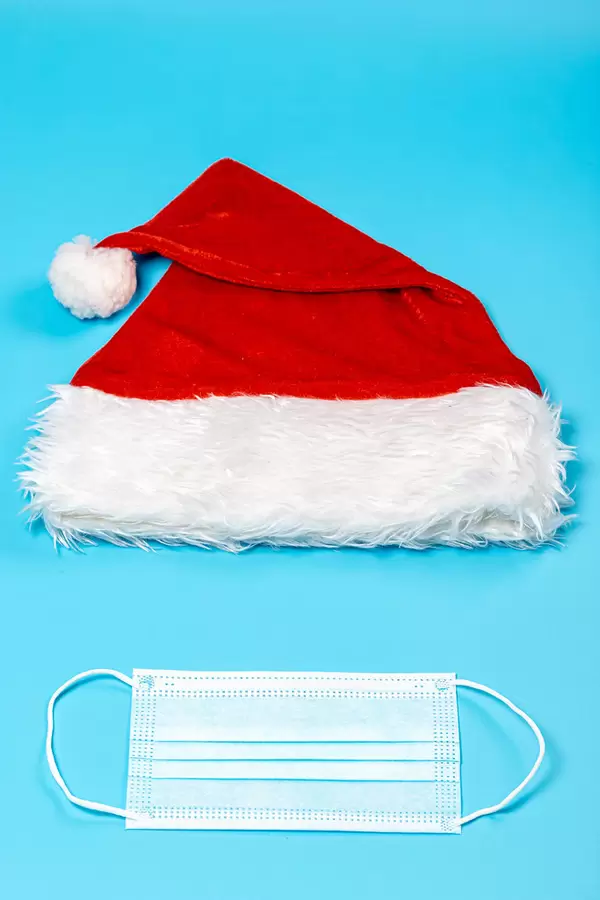 Medical mask and santa claus cap on blue background, top view