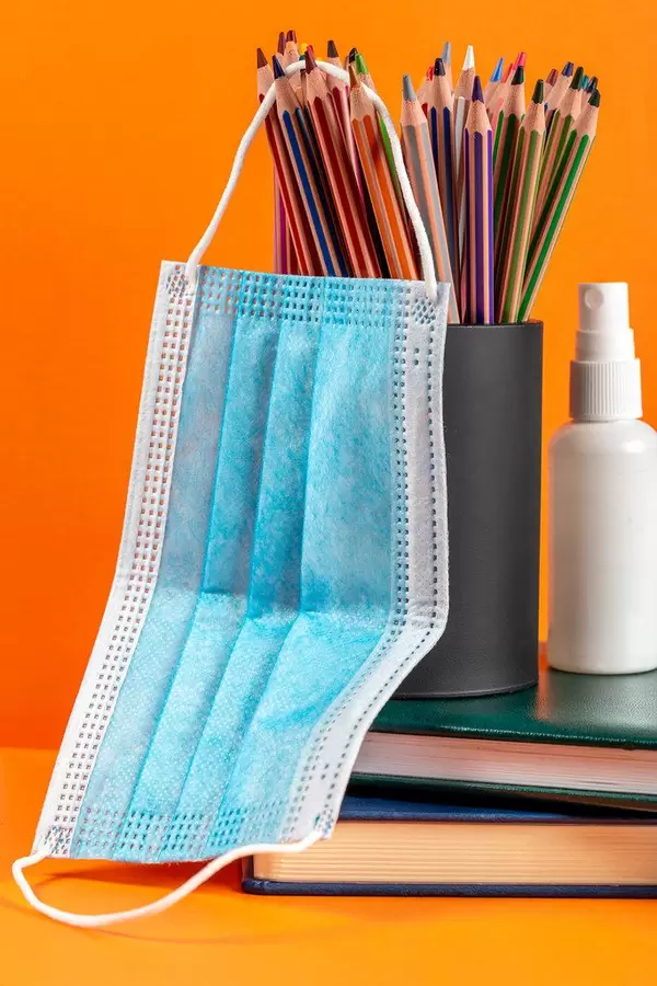 Medical mask hanging on colored pencils with orange background