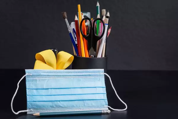 Medical mask with school supplies, bell and yellow ribbon on a black background