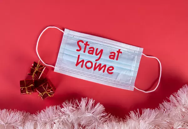 Medical protective face mask with Stay at Home text and Christmas decorations on red blue background