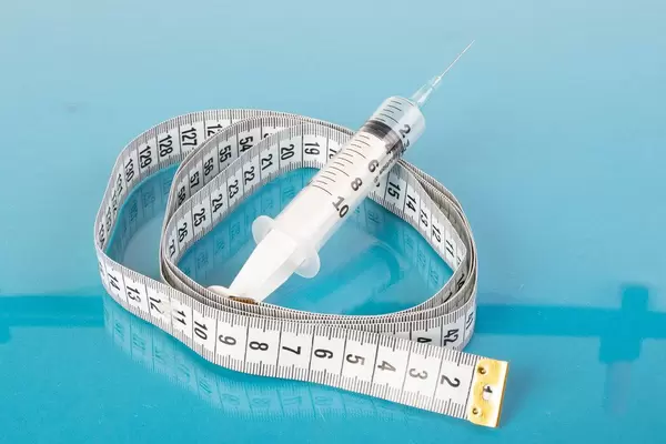 Medical syringe and tape measure on blue background