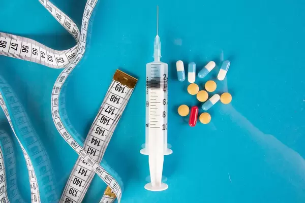 Medical syringe with pills and tape measure on blue background
