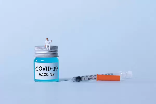 Medical workers sitting on a bottle with blue fluid and Covid-19 text
