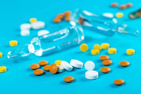 Medication background with multicolored pills and ampoules on blue