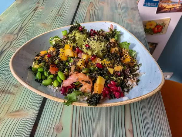 Meeresfrüchtensalat mit Mango, Bohnen, Reis mit kerniges Topping auf weiß-blauem Teller im Nahaufnahme