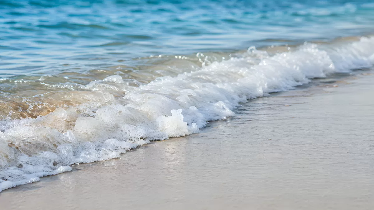 Meereswellen brechen sanft am weißen Sandstrand