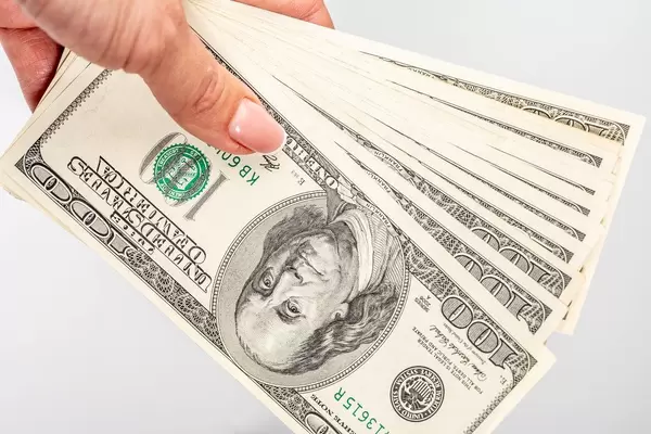 Mehrere einhundert Dollar-Scheine in einer Frauenhand vor weißem Hintergrund