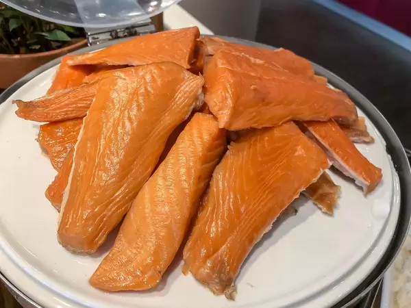 Mehrere Stücke Räucherlachs, gestapelt auf einem weißen Teller, am Hotelbüfett
