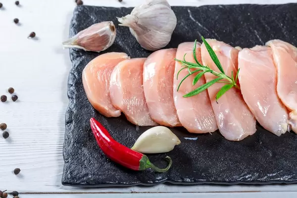 Mehrere Stücke rohe Hähnchenbrust mit Knoblauch, Chili, Rosmarin und Pfeffer auf Steinplatte