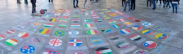 Menschen legen Münzen auf Ländeflaggen mit Kreide auf Pflaster gemalt  auf dem Kölner Weihnachtsmarkt