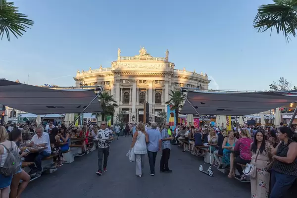 Menschen sitzen im Open-Air-Restaurant am Rathausplatz, Burgtheater im Hintergrund