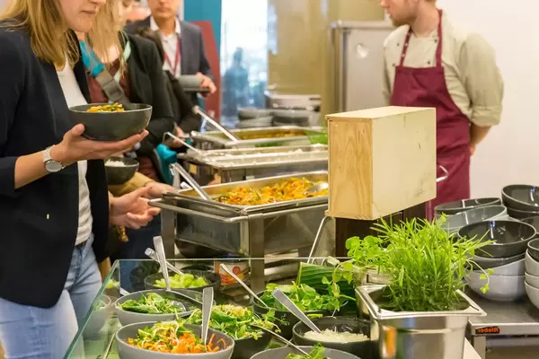 Menschen stehen in der Schlange vor dem ausgewogenes Mittagessen mit Salatbar am Büfett des Barcamps OMWest19 von AXA in Köln