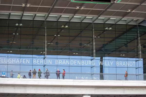Menschen vor dem BER Terminal 1 mit Schrift auf Glas "Flughafen Berlin Brandenburg Willy Brandt"