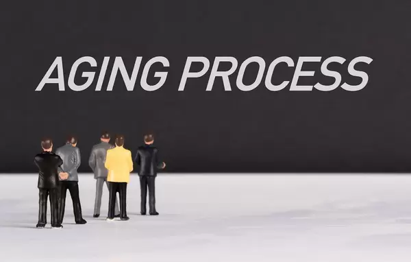 Menschenfiguren stehen vor einer schwarzen Wand mit  "Aging Process" als Text