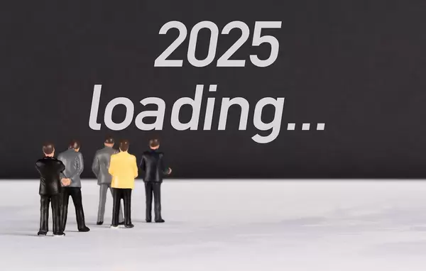 Menschenfiguren stehen vor einer Wand mit  "2025 loading" als Text