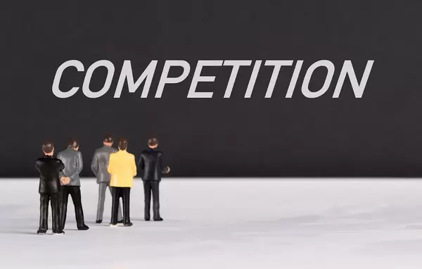 Menschenfiguren stehen vor einer Wand mit  "Competition" als Text