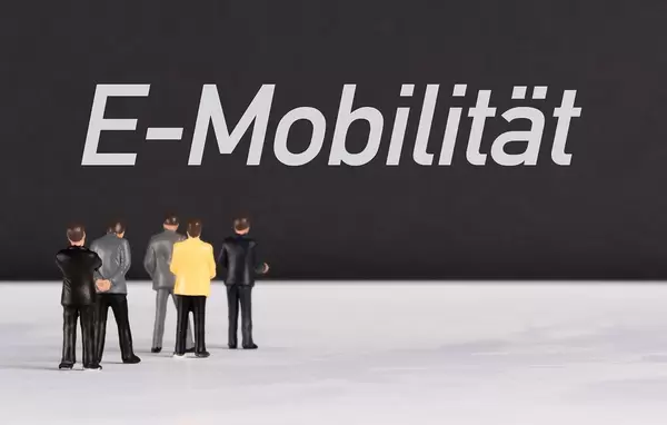 Menschenfiguren stehen vor einer Wand mit  "E-Mobilität" als Text