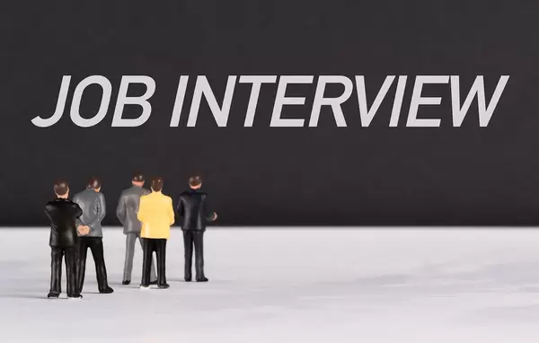 Menschenfiguren stehen vor einer Wand mit  "Job Interview" als Text