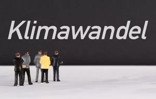 Menschenfiguren stehen vor einer Wand mit  "Klimawandel" als Text