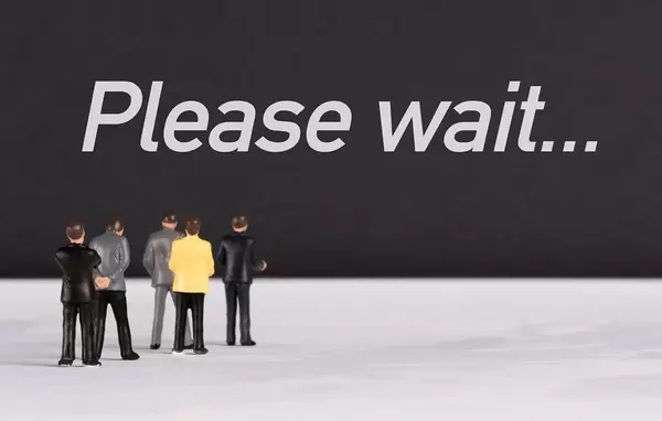 Menschenfiguren stehen vor einer Wand mit  "Please wait" als Text