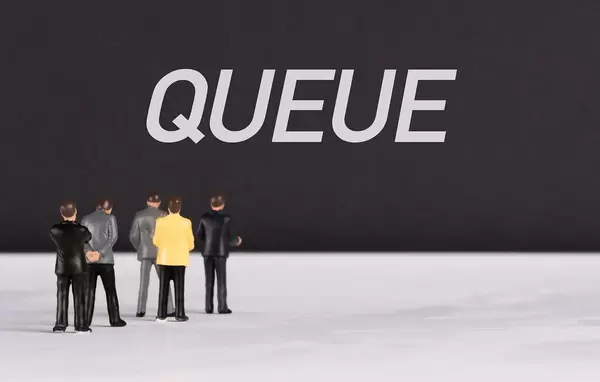 Menschenfiguren stehen vor einer Wand mit  "Queue" als Text