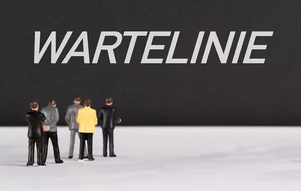 Menschenfiguren stehen vor einer Wand mit  "Wartelinie" als Text