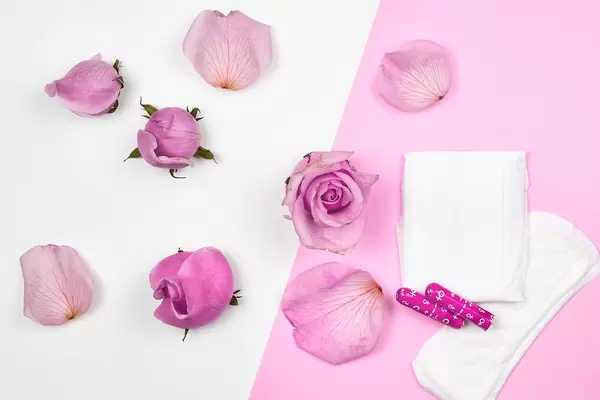 Menstrual cycle products: sanitary pad, panty liner and tampons on a pink-white background with roses