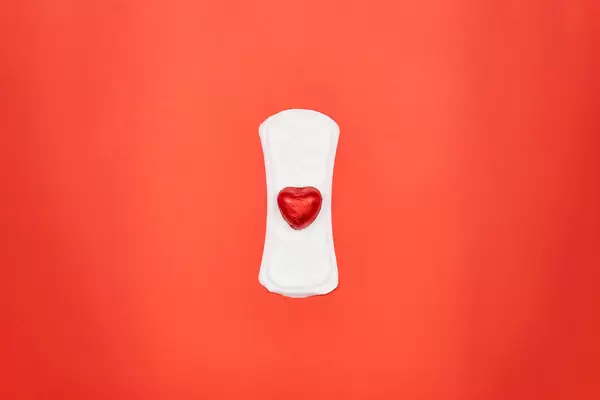 Menstruationsprodukte: eine Binde mit einem roten Schokoherz in der Mitte vor rotem Hintergrund