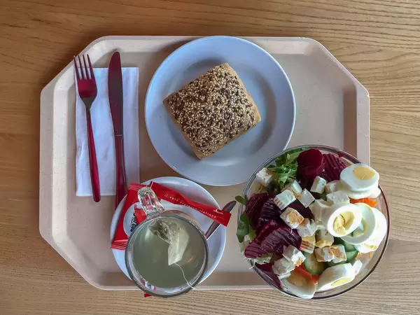 Menu in the canteen consisting of mixed salad with carrots, cucumber, rocket, beetroot, feta cheese and egg, with a wholemeal and tea, arranged with cutlery on a beige tray
