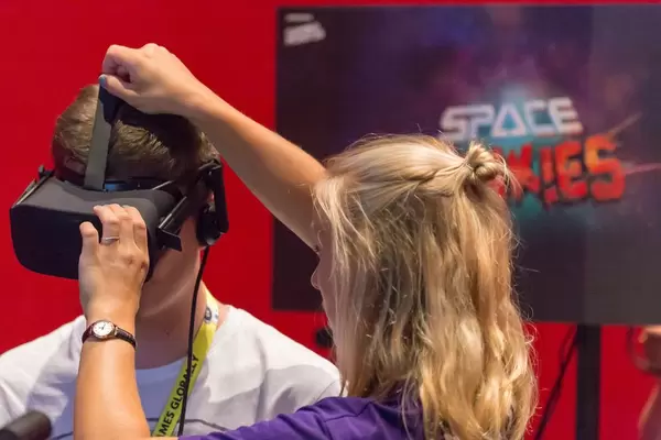 Messehostess hilft einem Besucher beim Aufsetzen des VR Headsets