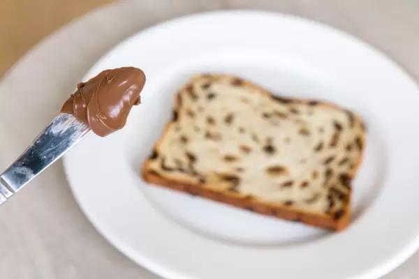 Messerspitze mit Nutella über Früchtekuchen auf weißem Teller