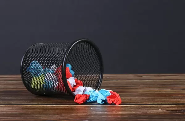Metal bin with crumpled paper on black background