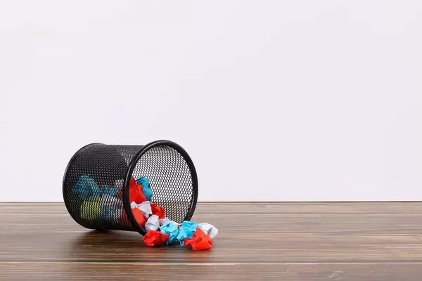 Metal bin with crumpled paper on white background