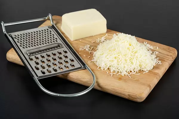 Metal cheese grater and mozzarella cheese on kitchen board