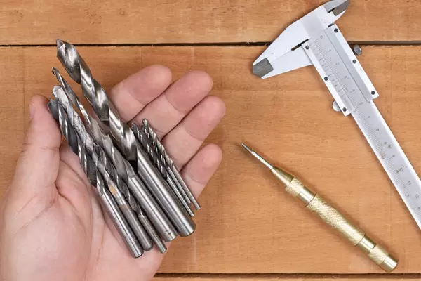 Metal Drills in the hand with measuring tools on the table