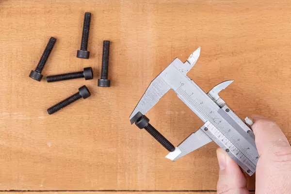 Metal nonius measuring Inbus screws above wooden table