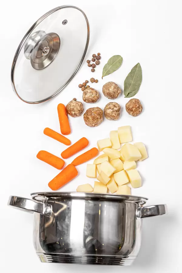 Metal saucepan with lid and raw ingredients for making soup