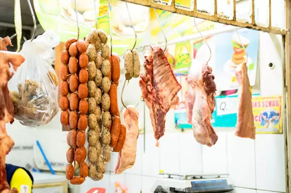 Metzgerstand an einem Markt mit an Fleischhaken aufgehängten Würsten und Fleischstücken