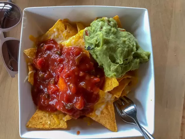 Mexican snack made of nachos covered with tomato dip and guacamole next to sunglasses on wooden table