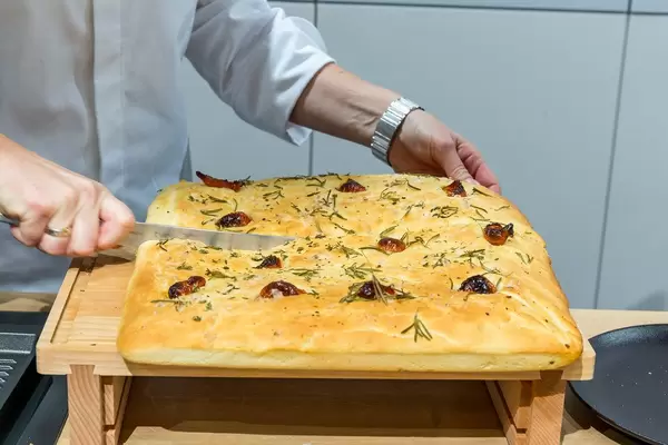 Miele-Backshow auf der IFA: Bettina Seitz von der Kochschule Münster schneidet selbstgebackenes Focaccia-Brot mit Rosmarin auf einem Holzbrettchen