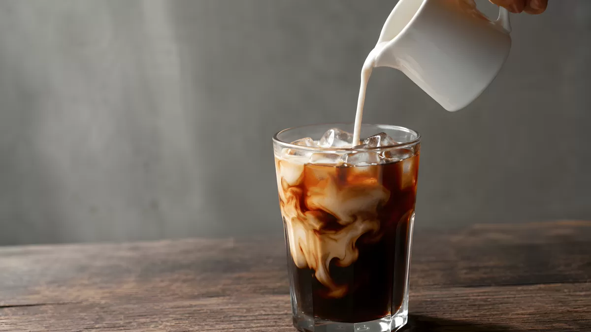 Milch wird in ein Eiskaffee-Glas gegossen