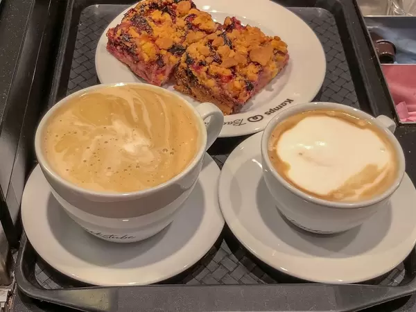 Milchkaffee und Cappuccino mit Pflaumen-Streuselkuchen auf einem Tablet in der Nahmaufnahme