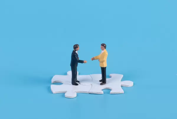 Miniature businessman handshaking on white jigsaw puzzle piece