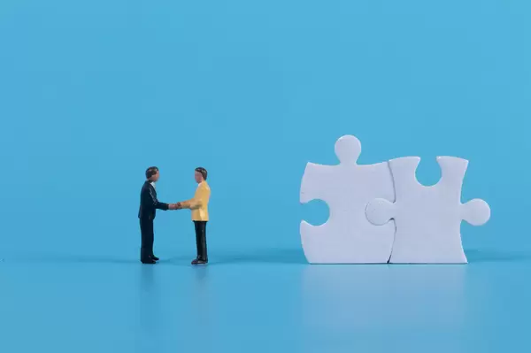 Miniature businessman handshaking with white jigsaw puzzle pieces