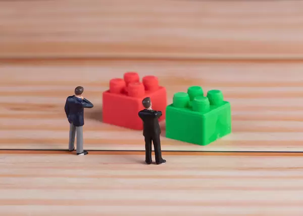 Miniature businessman standing in front of red and green plastic building blocks