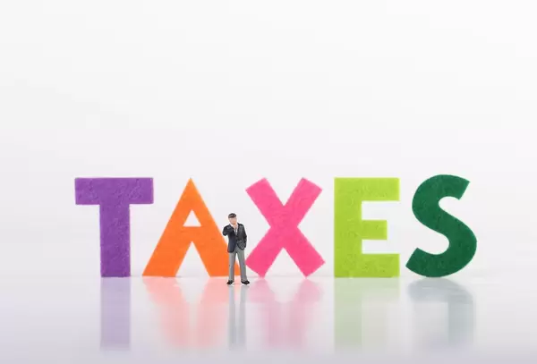 Miniature businessman standing in front of Taxes text on white background