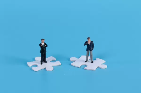 Miniature businessman standing on white jigsaw puzzle piece with blue background