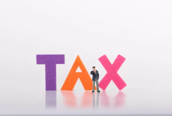 Miniature businessman with Tax text on white background