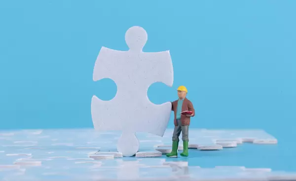 Miniature construction worker with jigsaw puzzle pieces on blue background