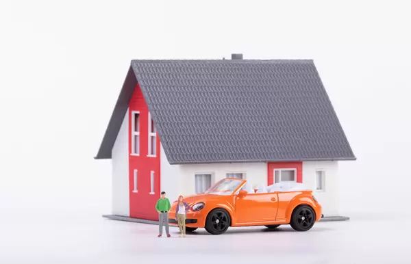 Miniature couple with orange car and a house on white background
